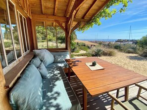 A wooden deck with a sofa and a table, overlooking a beach with a fence and vegetation. - Idyllic beach house with fantastic views A0081 (Lège-Cap-Ferret)