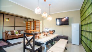 A modern living room with a sofa, dining table, chairs, and a television.