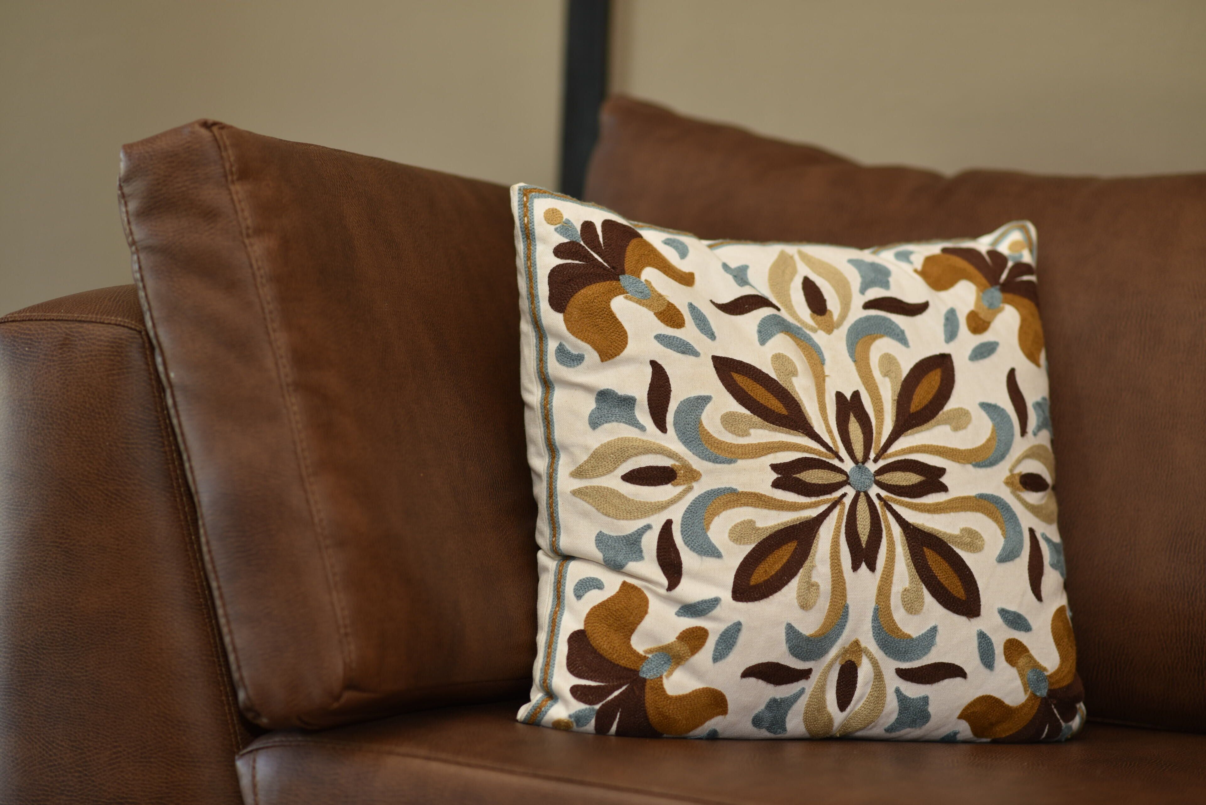 A brown leather sofa with a decorative pillow featuring a floral pattern.