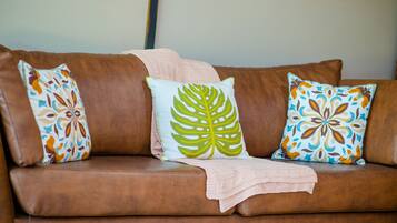 Un sofá de cuero marrón con tres almohadones estampados y una manta tejida.