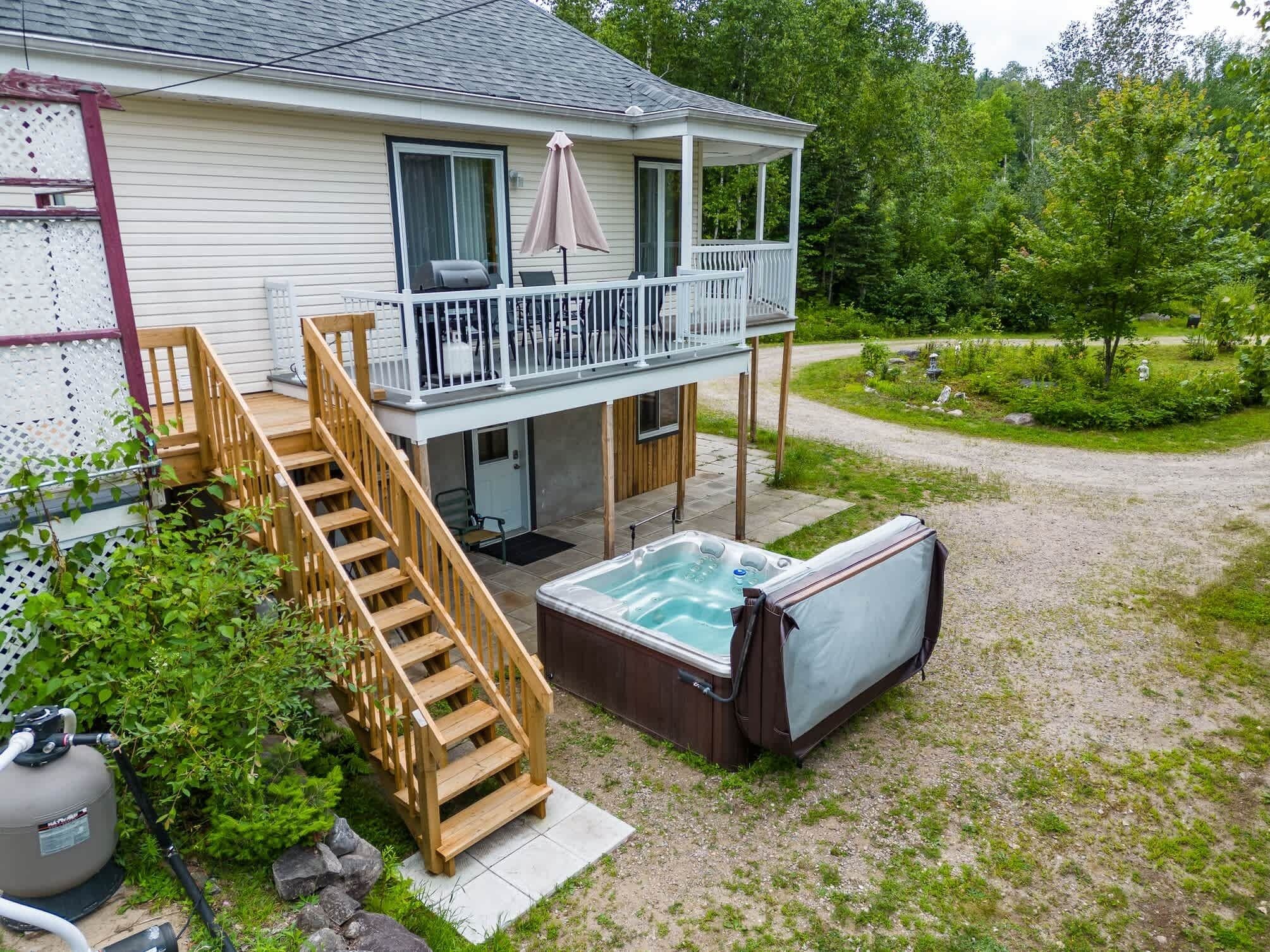 A two-story house with a covered patio, a hot tub, and a wooden staircase leading to the upper level.