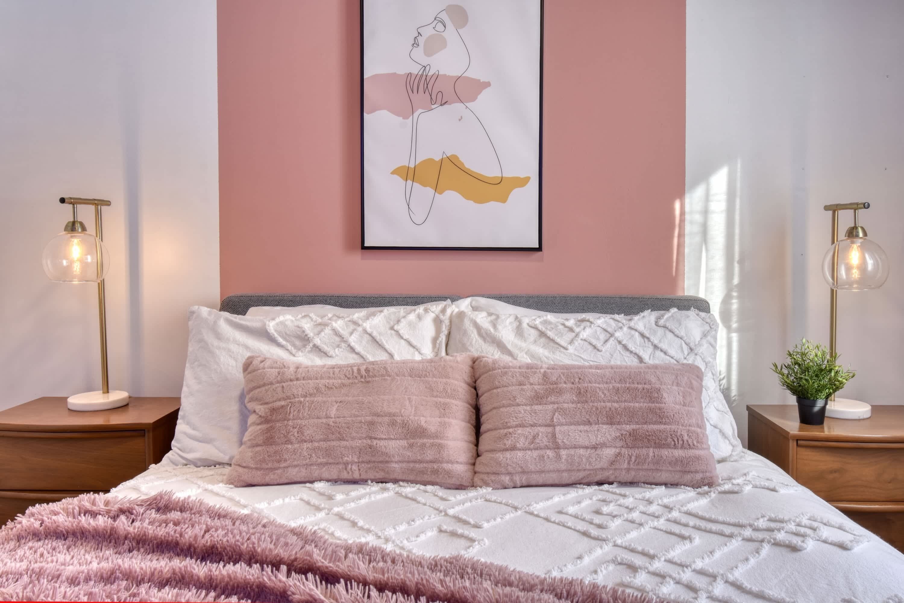 A bedroom with a bed, two bedside tables, a wall-mounted artwork, and a window.