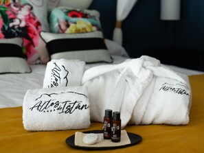 A hotel room with a bed, pillows, and a set of white towels with embroidered text. There are also two small bottles and a soap bar on a tray. - Hotel Altos de Istán (Istan)