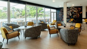 A modern indoor seating area with leopard print furniture, large windows offering a view of greenery and a building, and a mural on the wall. - Hotel Altos de Istán (Istan)