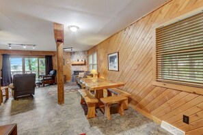 A wooden interior with a dining area, stone fireplace, and large windows.
