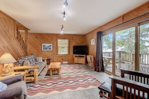 A wooden interior with a sofa, table, and TV, a patterned rug, and a balcony with a railing. - Pine Bay Lodge - Lakefront (Wisconsin Dells)