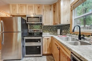 A kitchen with wooden cabinets, stainless steel appliances, a tiled backsplash, and a window with a view of trees.