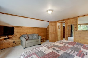 A bedroom with a wooden ceiling, a television on a wooden stand, a grey sofa with cushions, a quilted bedspread, and a wooden wardrobe with a 'WELCOME TO' sign. - Pine Bay Lodge - Lakefront (Wisconsin Dells)