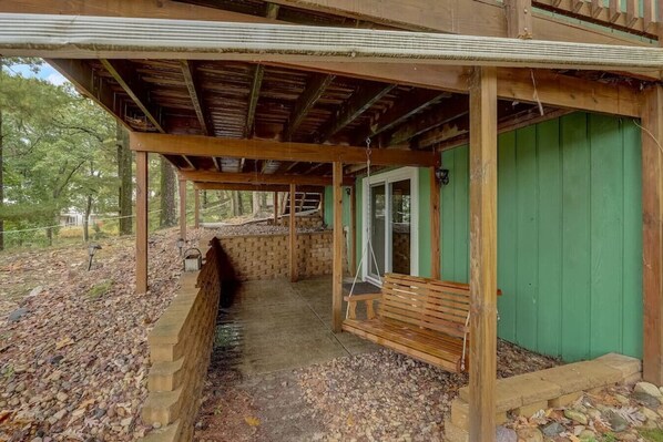 A covered porch with a bench, wooden beams, and a green wall.