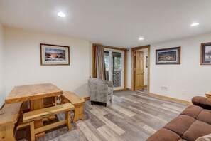 A room with a wooden dining table, a sofa, and a chair. There are two doors leading to another room.
