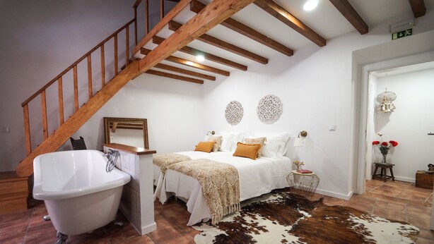 A bedroom with a wooden staircase, a white bathtub, a bed with white bedding and a cowhide rug. - Marias Guesthouse beja (Beja)