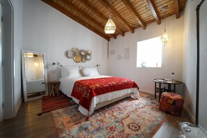 A bedroom with a wooden ceiling, a bed with a red blanket, a patterned rug, a small round table, and a window with natural light. - Marias Guesthouse beja (Beja)