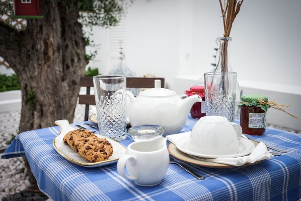 A table set with a teapot, sugar bowl, creamer, cookie, and a glass pitcher, with a tree and a red birdhouse in the background. - Marias Guesthouse beja (Beja)