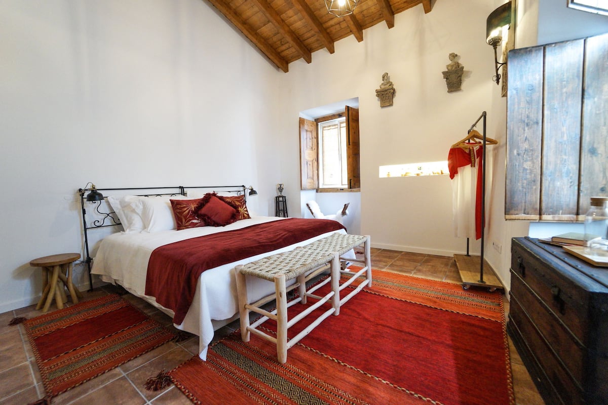 A bedroom with a bed, bench, dresser, and a window with shutters.