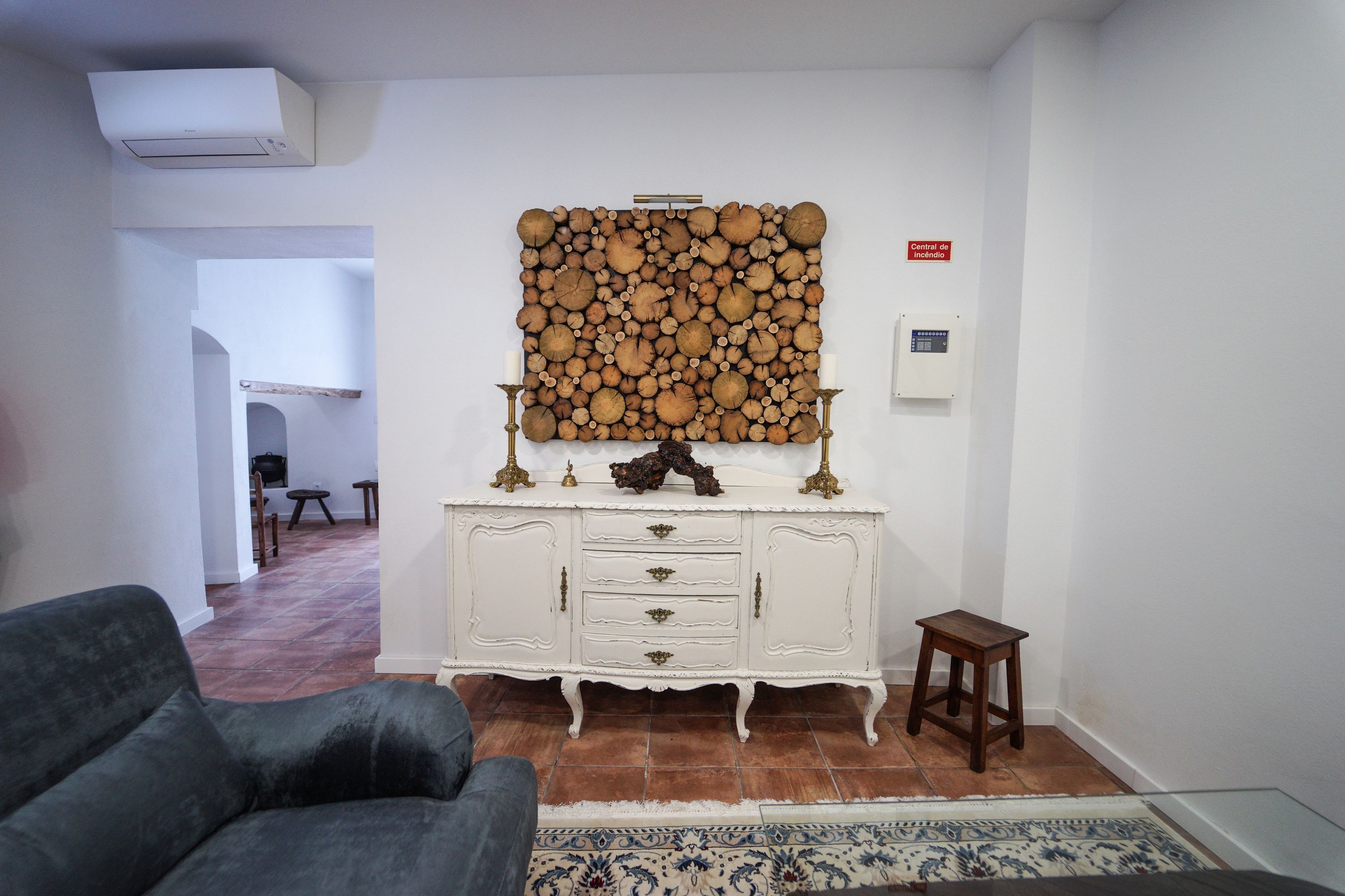 A living room with a white cabinet, a decorative wall piece, a small wooden stool, and a patterned rug.