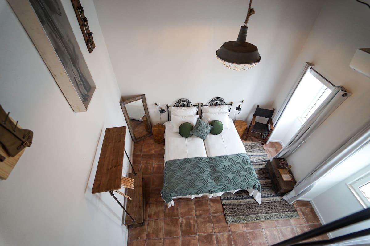 A bedroom with a bed, a hanging light fixture, a wooden bench, and a window.