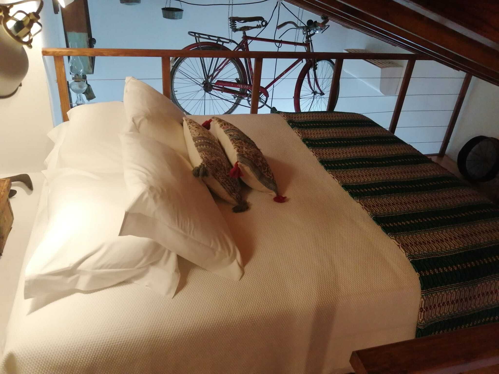 A bed with white linens and two decorative pillows, a striped rug, and a bicycle in the background.