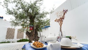A table set with a teapot, sugar bowl, creamer, and a cookie, with a blue tablecloth and a vase of dried flowers. - Marias Guesthouse beja (Beja)