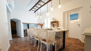 A dining area with a table set for four, surrounded by white chairs. There is a wooden cabinet with glassware and a window above the door. - Marias Guesthouse beja (Beja)