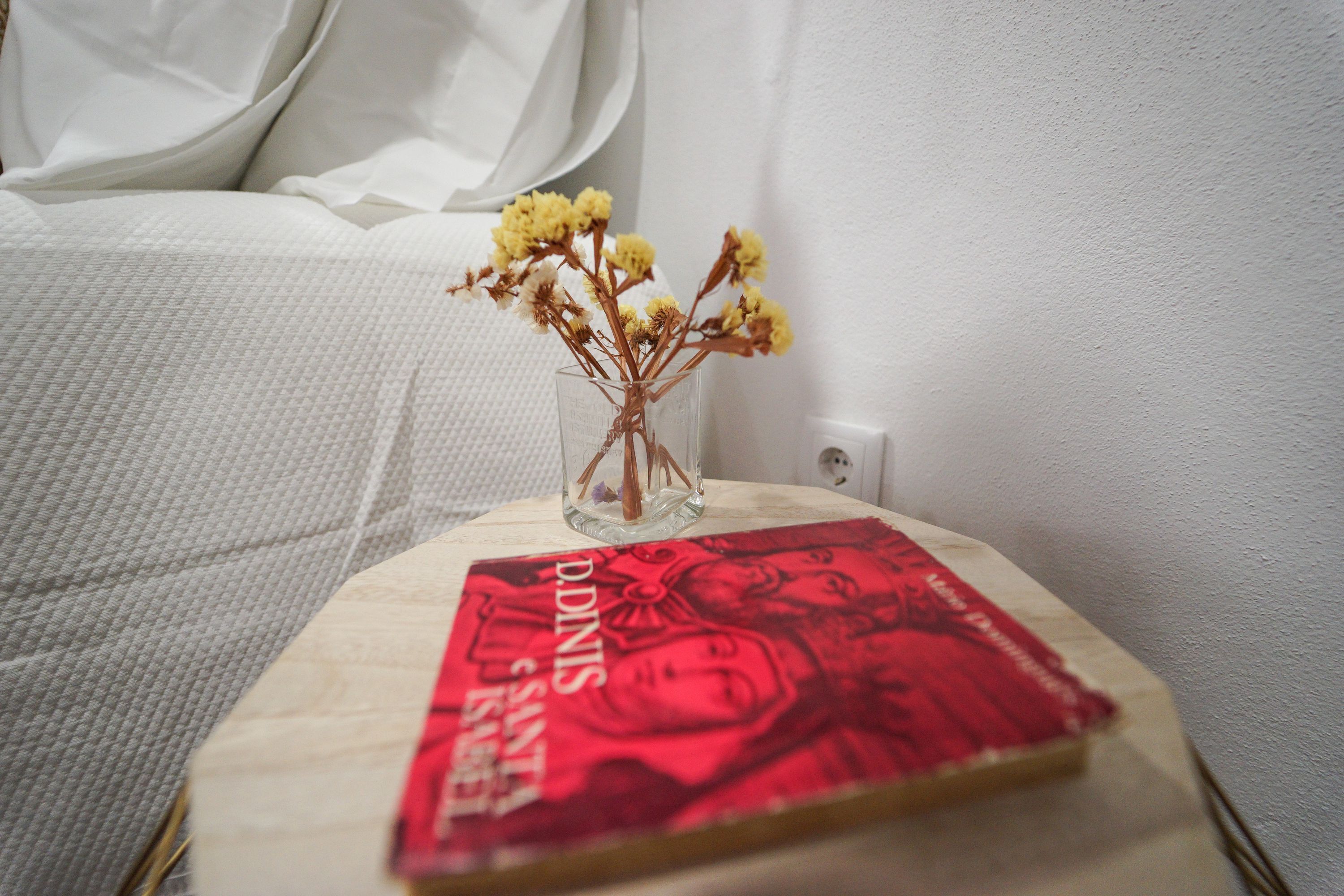 A book titled "Dundie Awards" on a wooden table next to a white bed with a white pillow.
