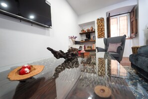 A modern living room with a glass coffee table, a wooden side table with a red object, a grey armchair, and a blue sofa. - Marias Guesthouse beja (Beja)