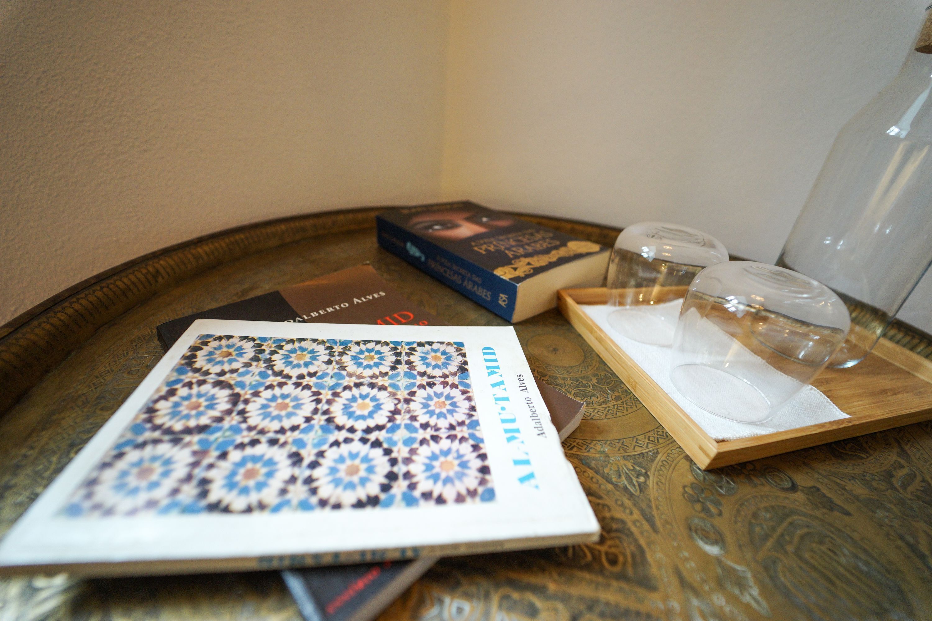 A tray with a book, two glasses, and a bottle on a patterned table.