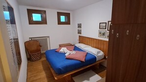A bedroom with a bed, a chair, a radiator, and a wooden wardrobe. - Appartamento Cervinia Fronte Funivie (CERVINIA)