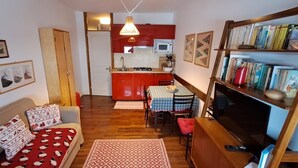 A compact living space with a kitchenette, a dining area, and a seating area with a sofa and a TV. - Appartamento Cervinia Fronte Funivie (CERVINIA)
