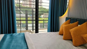 Habitación de hotel con cama, cortinas azules y vista a un parque infantil por la ventana.