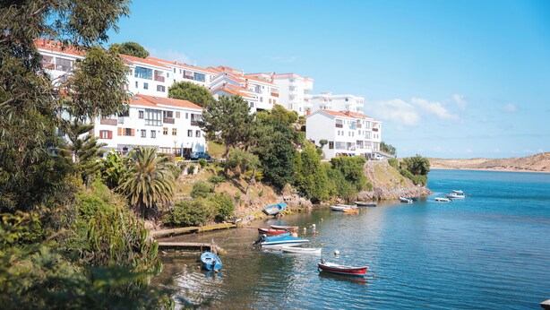 A coastal residential area with multi-story buildings, a calm sea, and several small boats anchored near the shore.