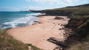 A coastal beach with a sandy shore, rocky cliffs, and a clear blue sky.