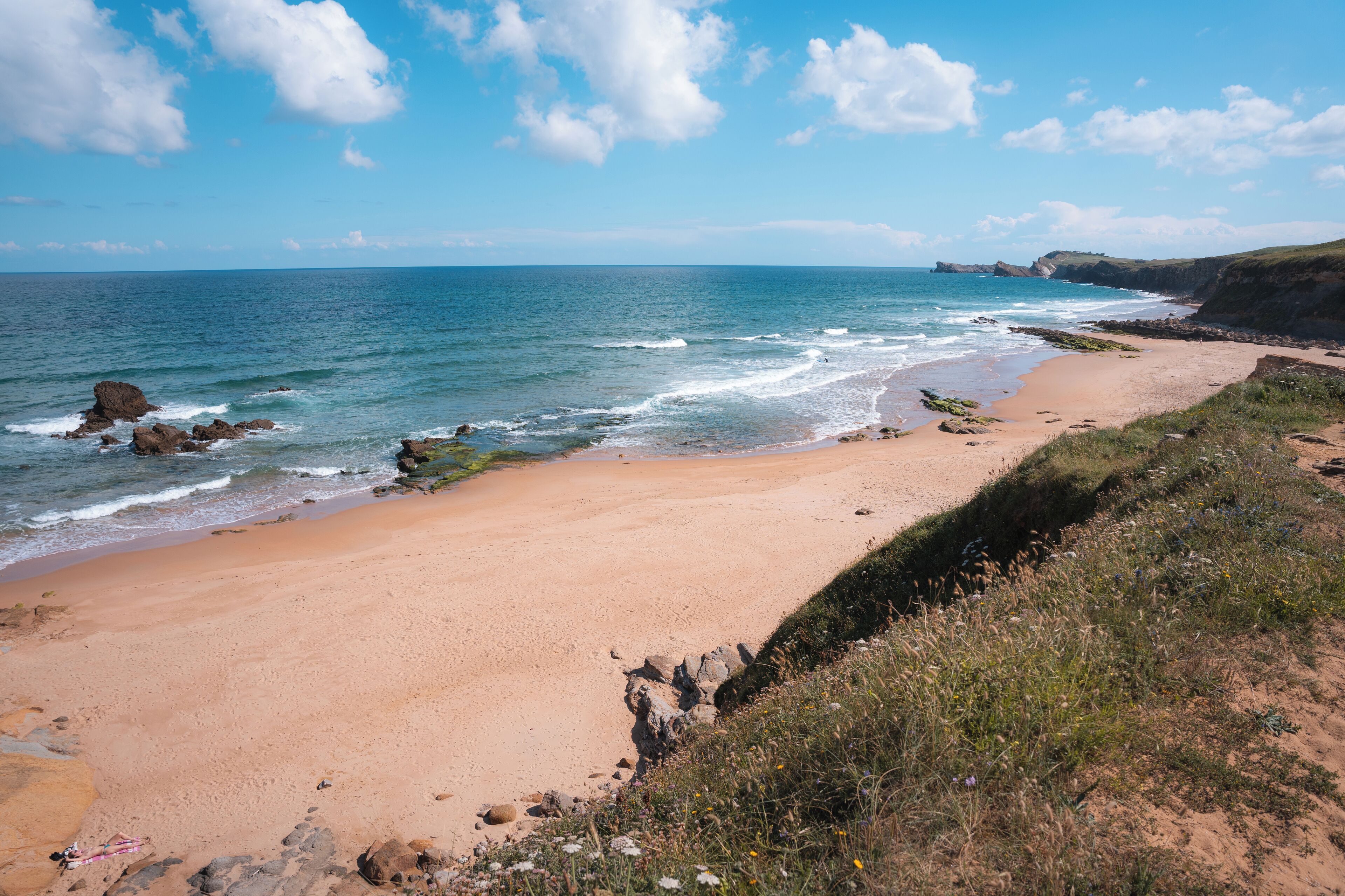 A coastal beach with a sandy shore and rocky outcrops.