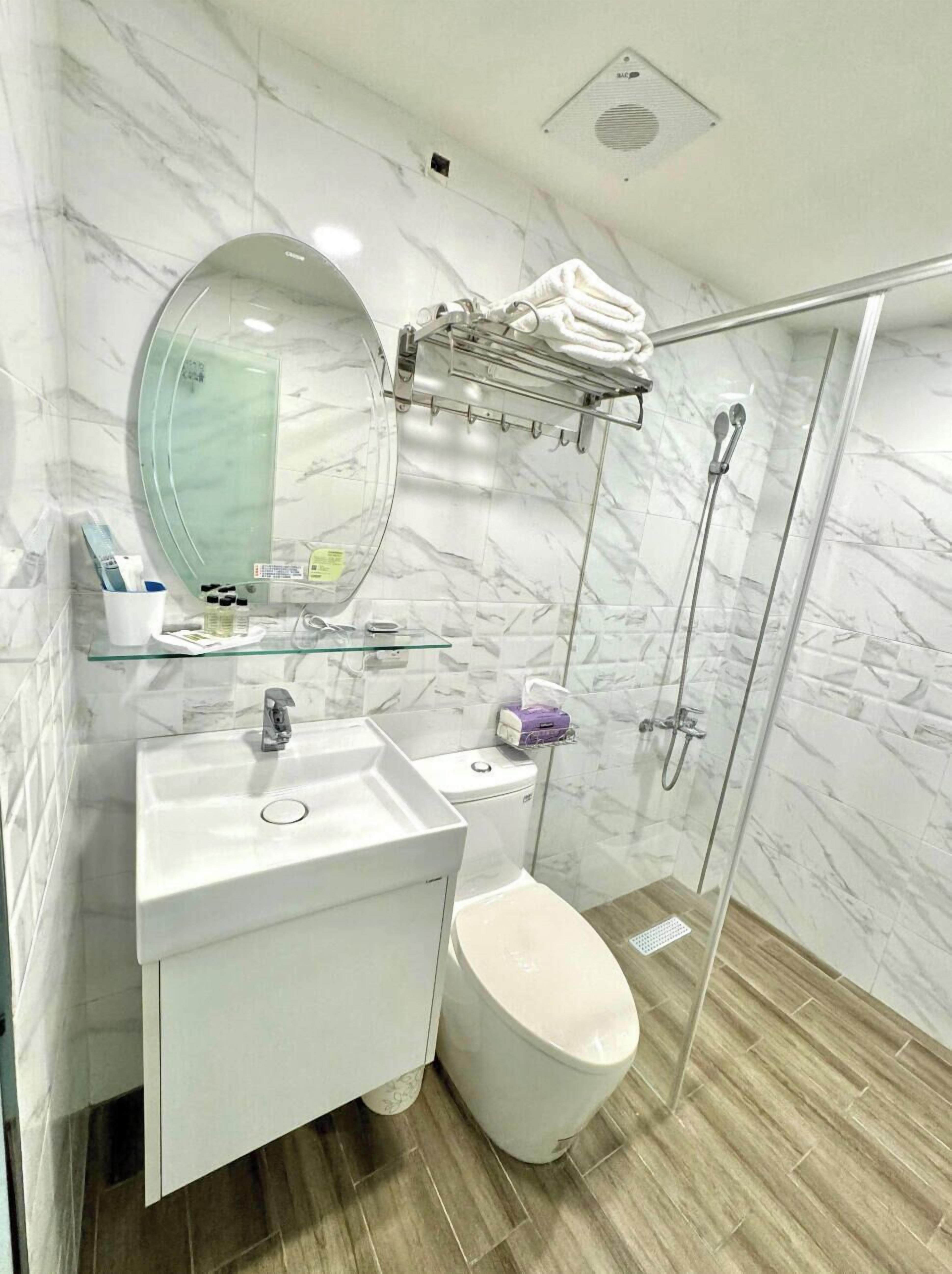 Un baño moderno con pared de mármol, cabina de ducha de vidrio, lavamanos blanco y un inodoro.