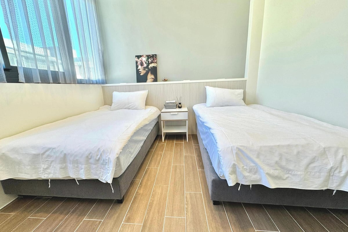 A twin room with two single beds, a nightstand, a small table, and a painting on the wall.