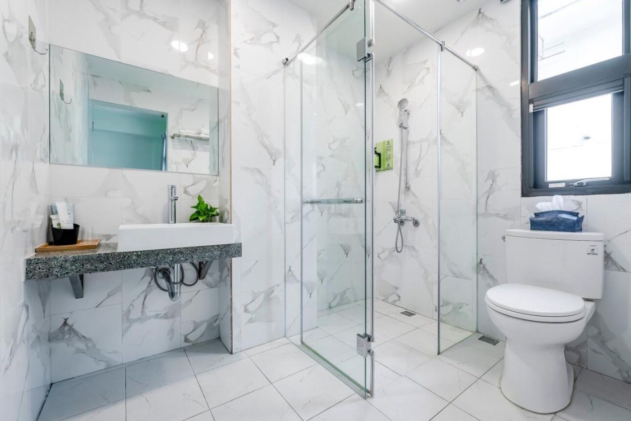 Un baño moderno con ducha de vidrio, inodoro blanco y suelo de mármol.