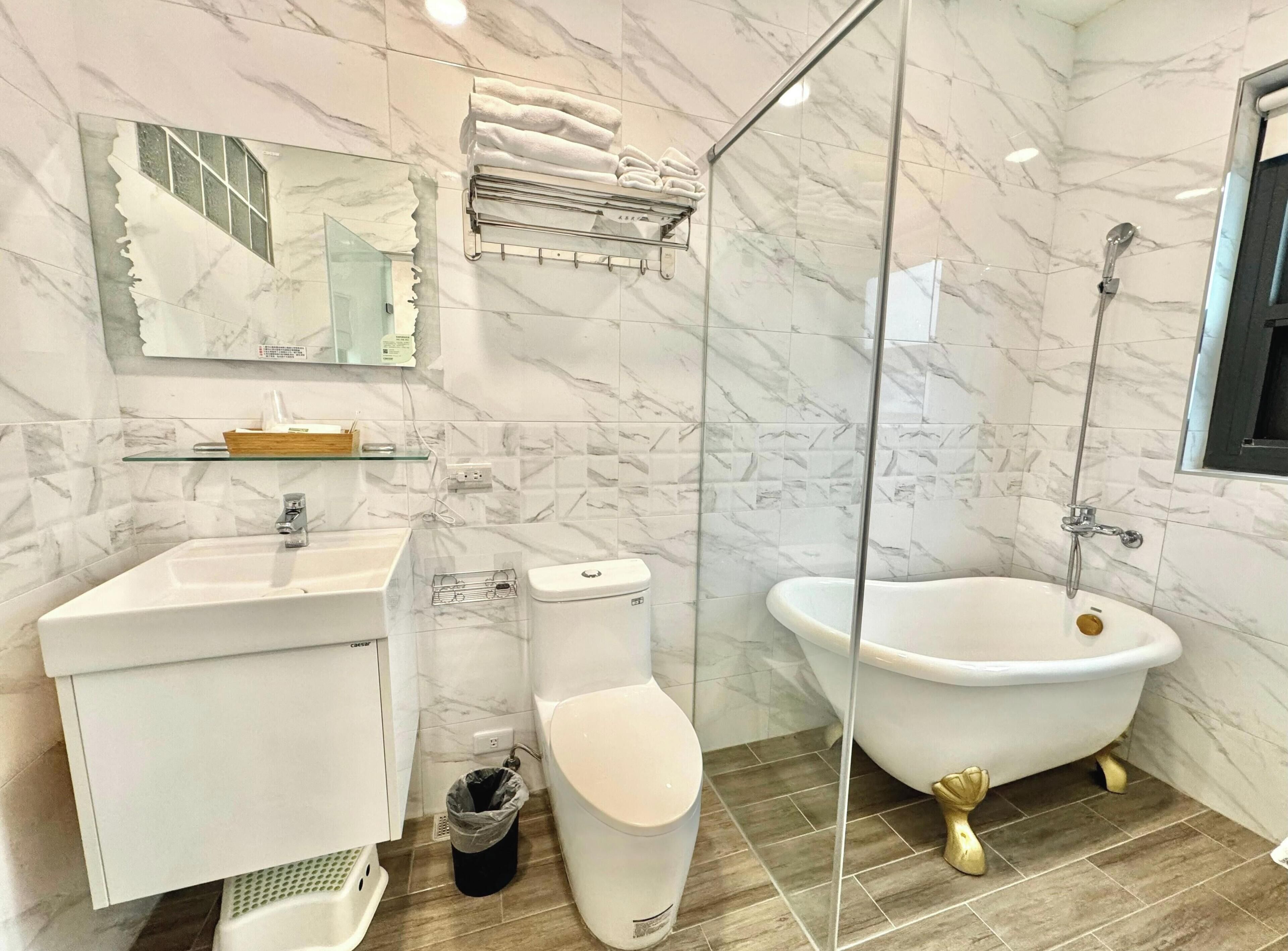 Un baño con lavamanos blanco, inodoro y bañera tipo patas de león. Cuenta con cabina de ducha de vidrio y paredes de mármol.