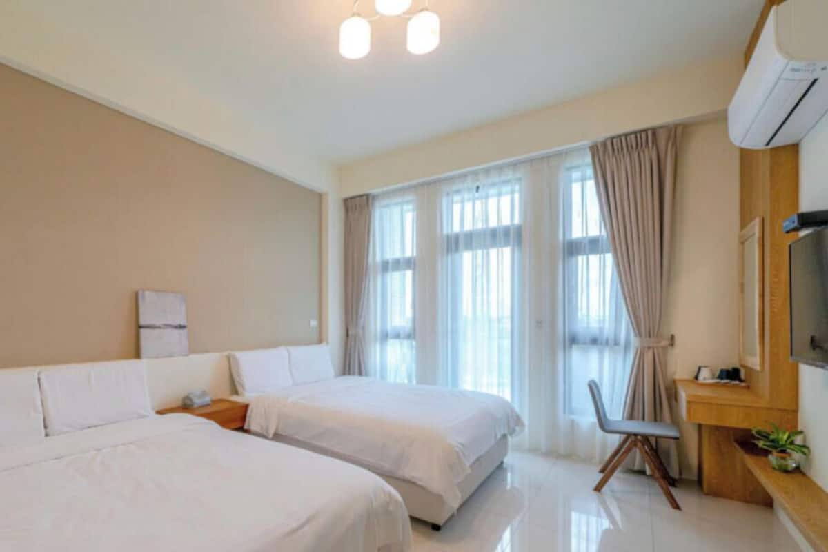 A hotel room with two beds, a desk, a chair, a TV, and a window with curtains.