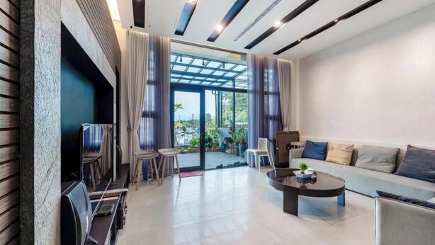 A modern living room with a sofa, coffee table, and TV. There is a sliding glass door leading to an outdoor area with plants. - Miguo Homestay (Wujie)