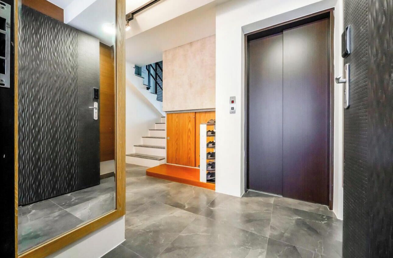 A modern hallway with a staircase, a wooden cabinet, and a dark door.