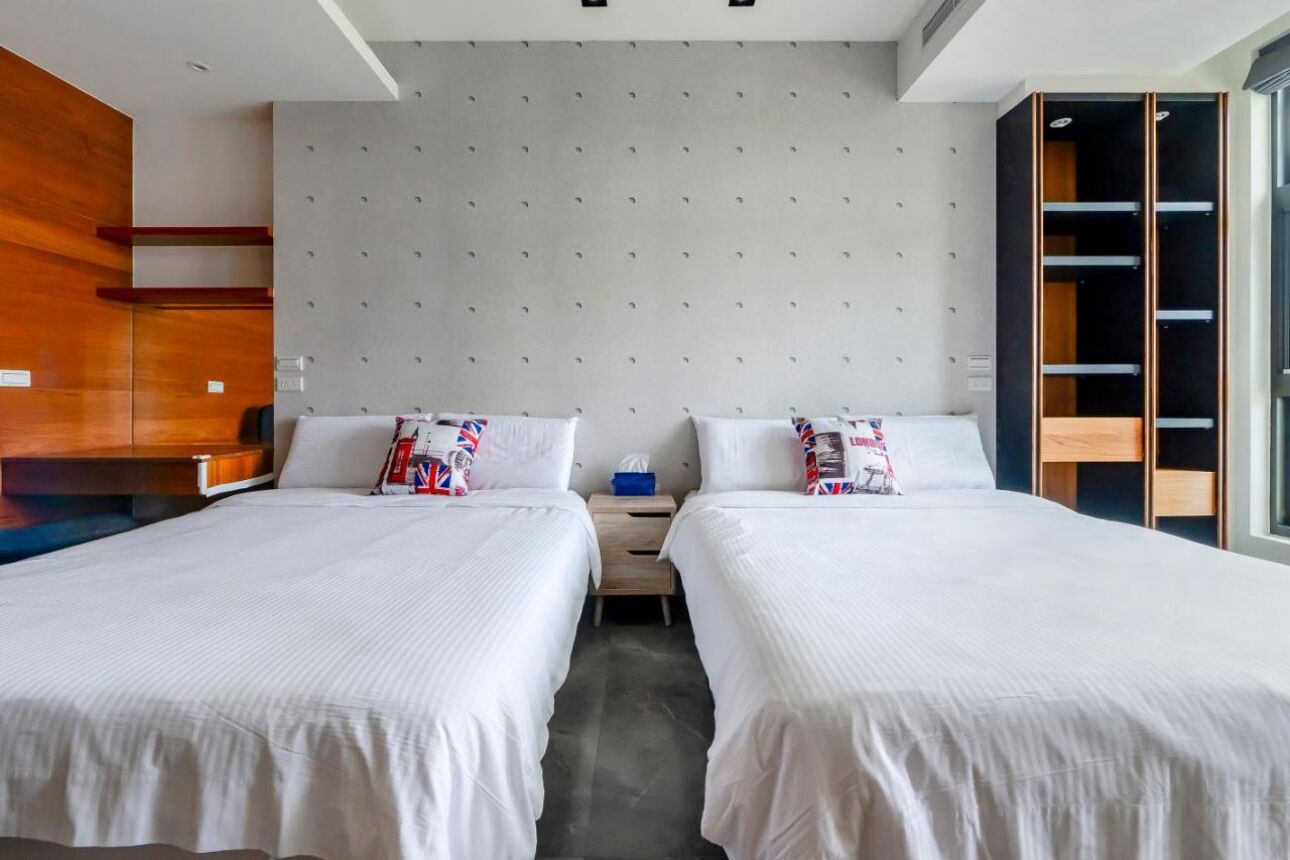 A hotel room with two beds, a wardrobe, and a small bedside table.