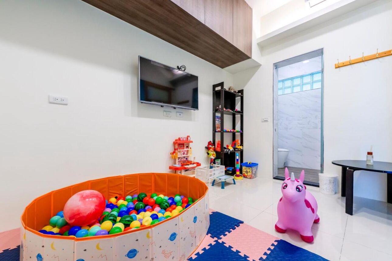 Zona de juegos infantiles con piscina de pelotas, juguetes y un caballo de juguete rosa.