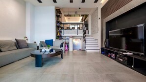 A modern living room with a sofa, coffee table, and TV. There is a staircase leading to an upper level with kitchen appliances. - Miguo Homestay (Wujie)