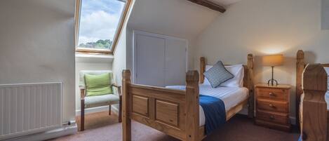 A bedroom with a wooden bed, a nightstand, a chair, a radiator, and a window with a view of greenery.