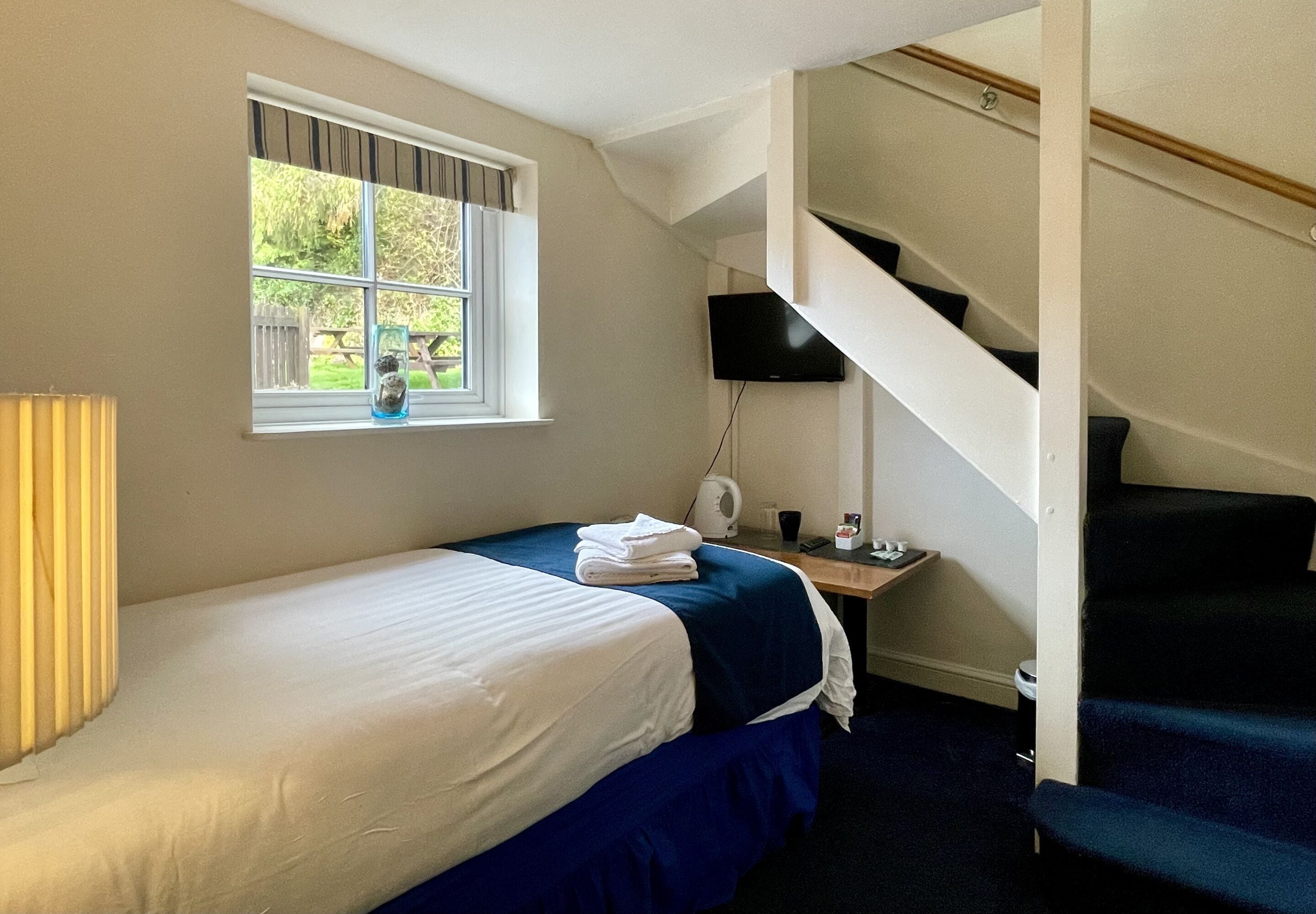 Un dormitorio con cama, ventana, escritorio, lámpara y escalera.