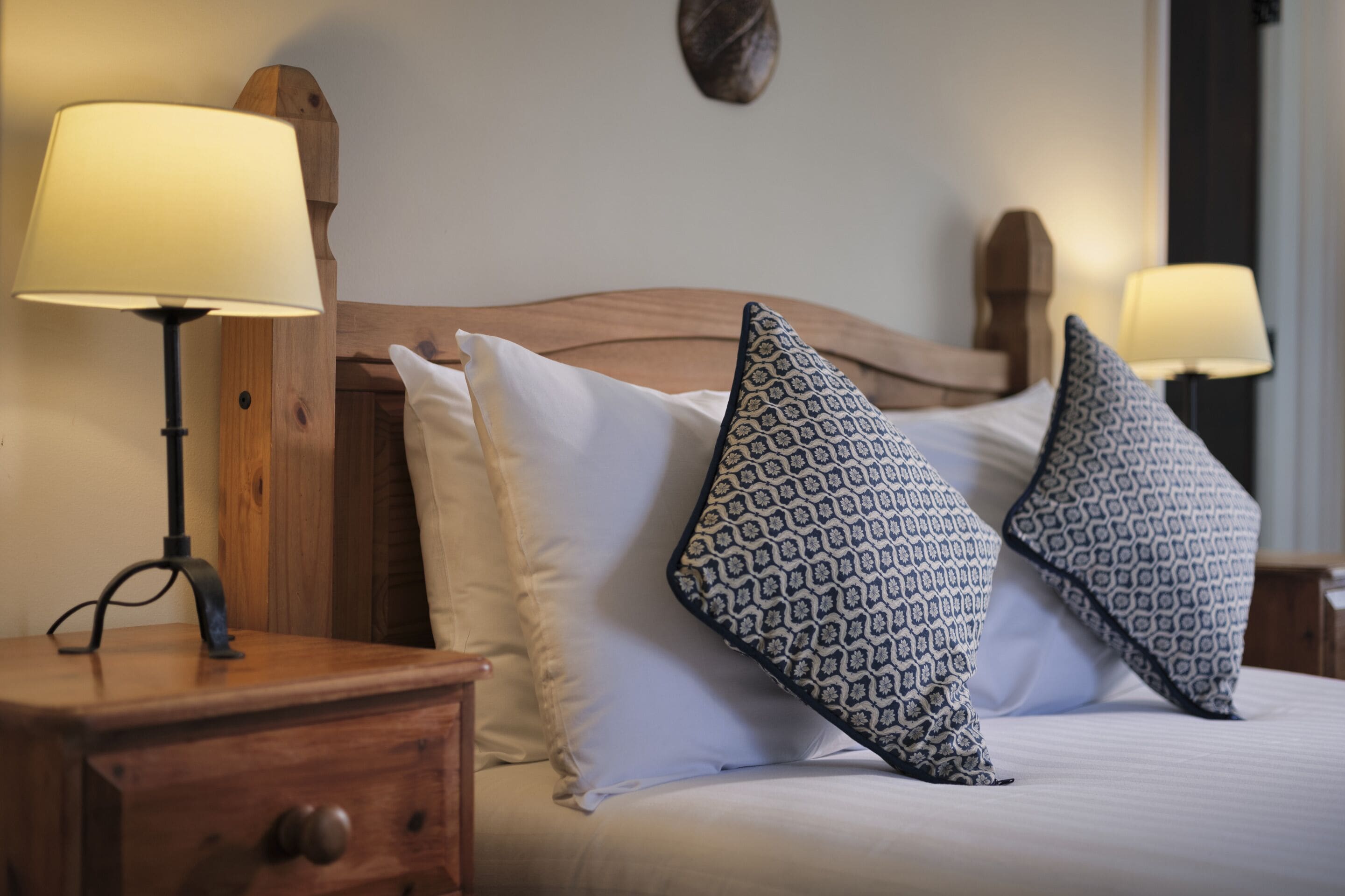 A neatly made bed with patterned pillows, a wooden headboard, and bedside lamps on a nightstand.