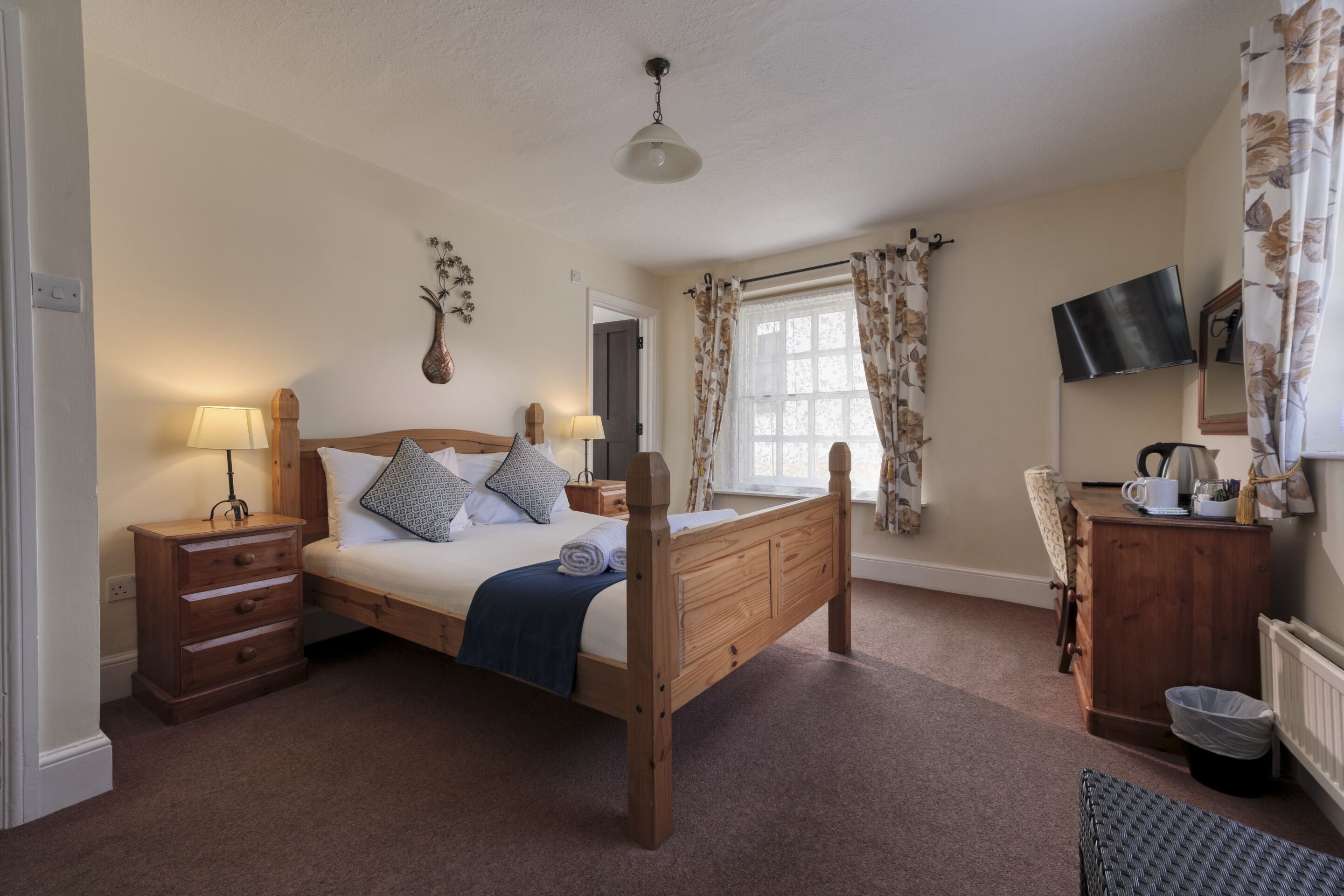 A bedroom with a wooden bed, bedside tables, a desk, a chair, a TV, and a window with curtains.