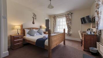 A bedroom with a wooden bed, bedside tables, a desk, a chair, a TV, and a window with curtains.