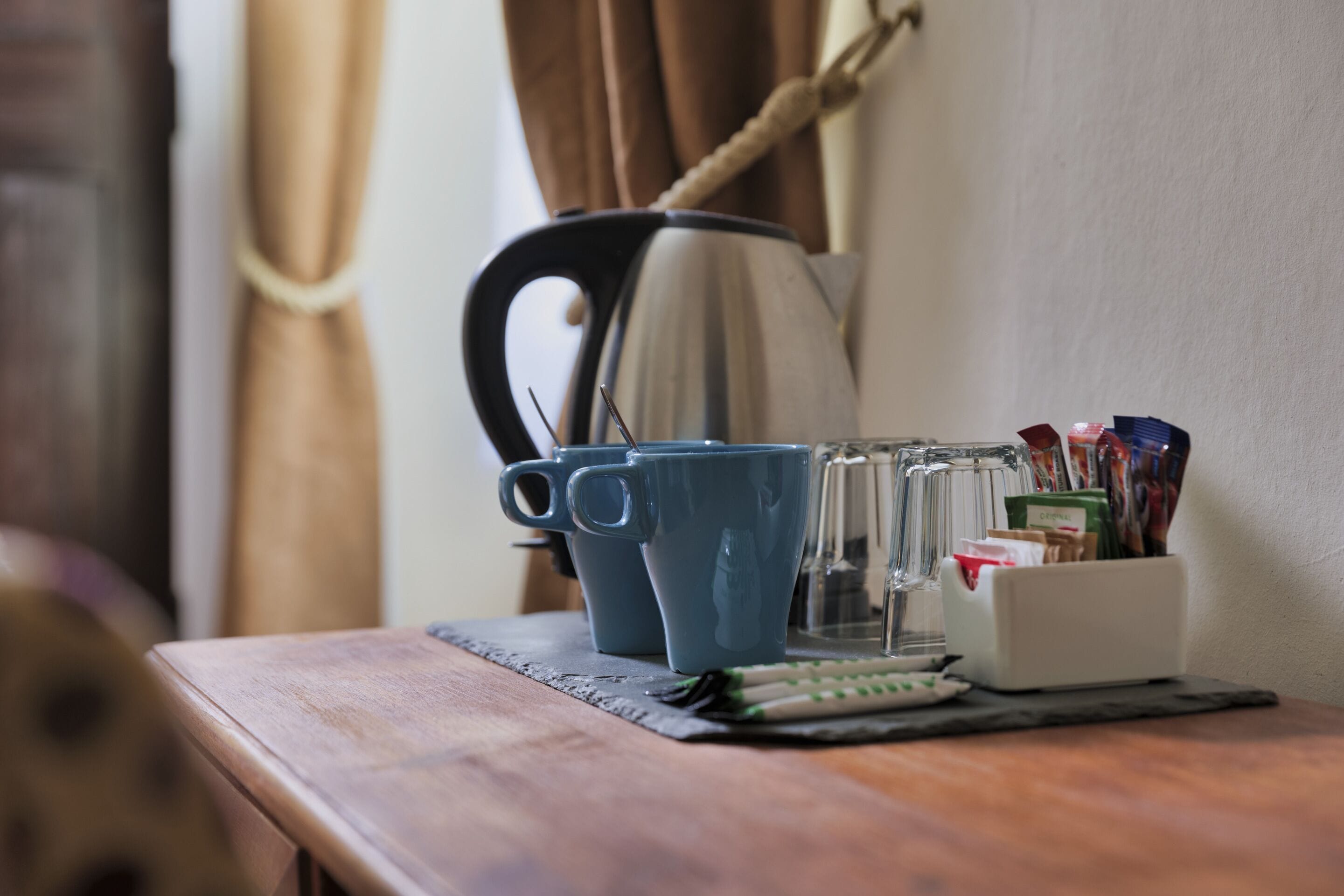 Ett träbord med en kaffebryggare, två blå muggar, en glasburk och en behållare med pennor och andra kontorsartiklar.