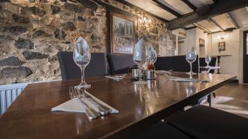 A dining table set with wine glasses, a pitcher, and cutlery in a room with stone walls and wooden beams.