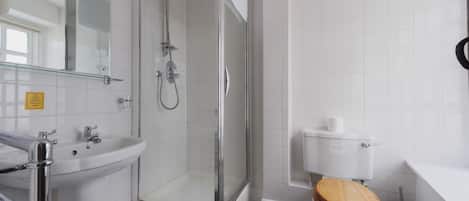 Un baño moderno con ducha envuelta en vidrio, un lavamanos blanco y un inodoro de madera.